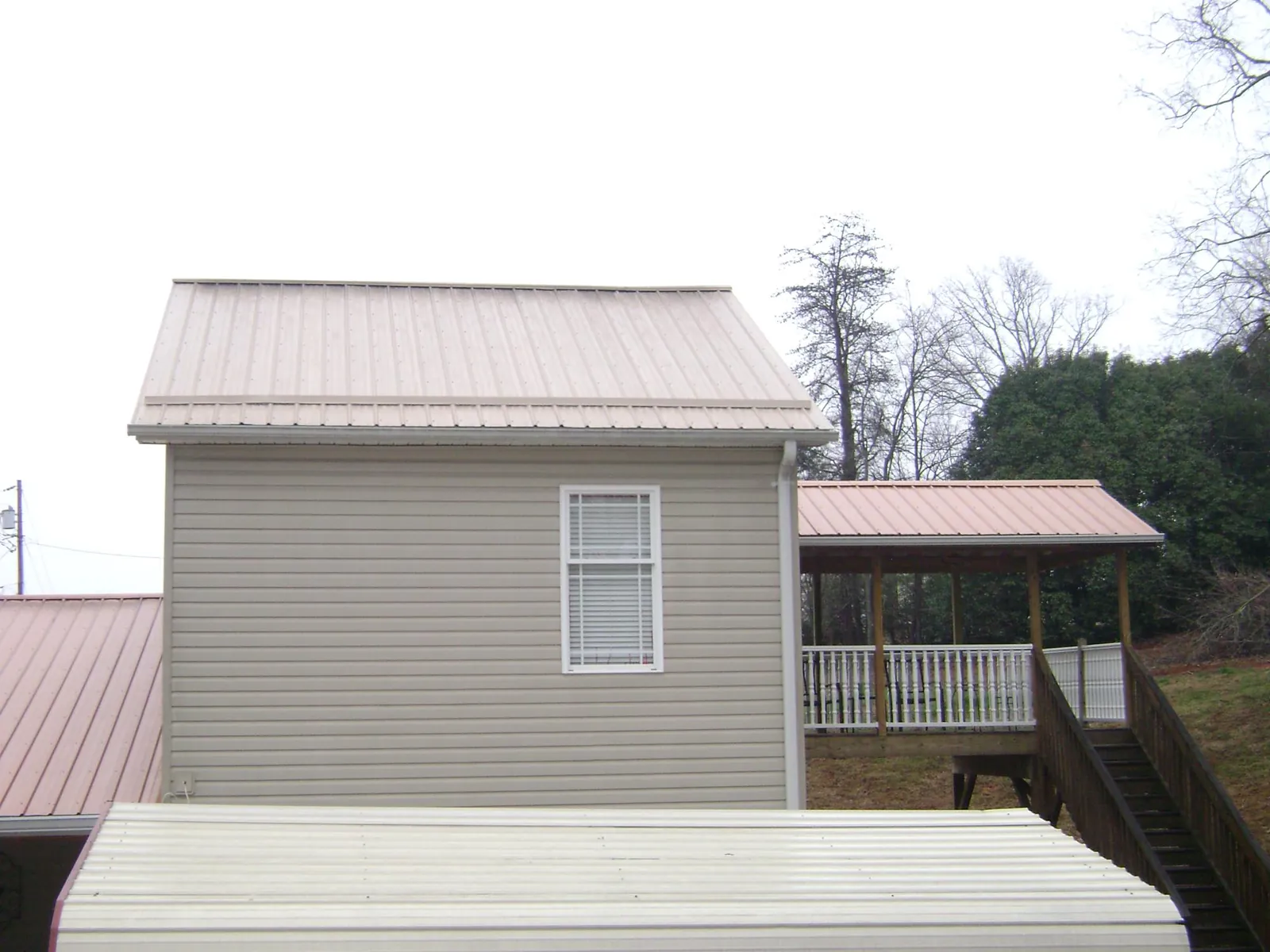 Tan metal roofs on a two story addition and attached porch, from a Roof Replacement job in Troy